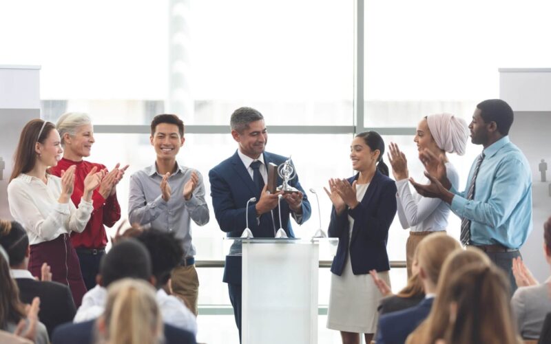 businessman-holding-award-on-podium-with-colleagues-at-business-seminar.jpg